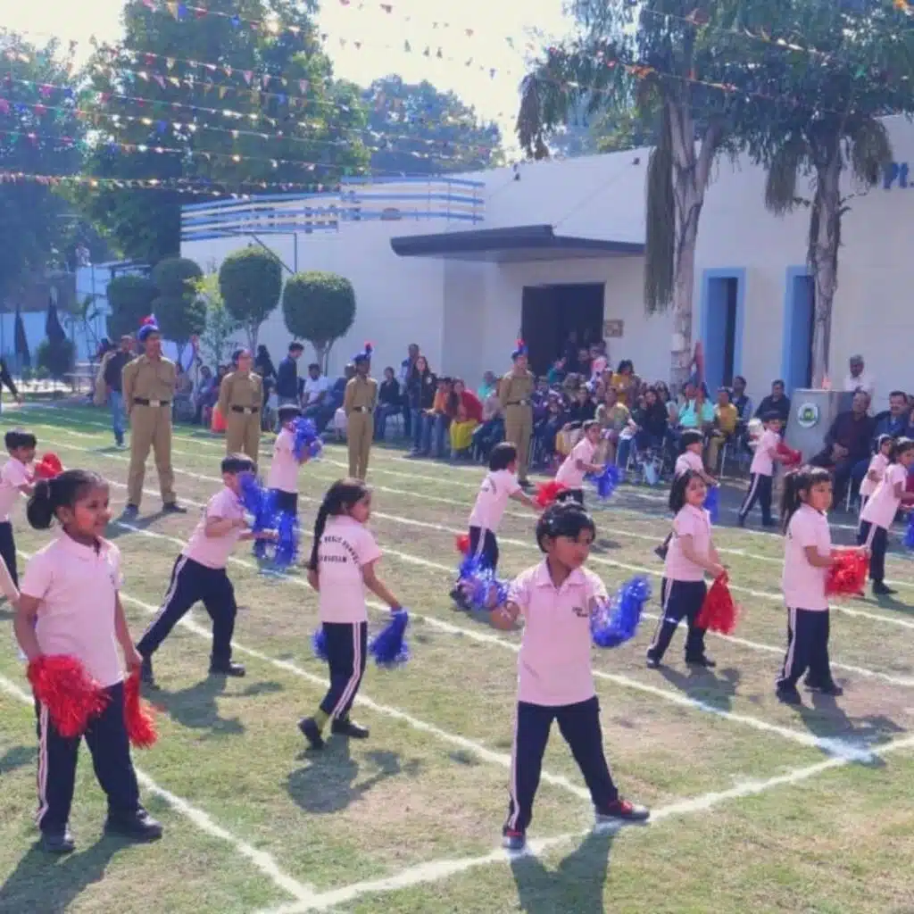 Children participating in an outdoor school sports event, performing a cheerleading or drill routine on a marked field with spectators watching.