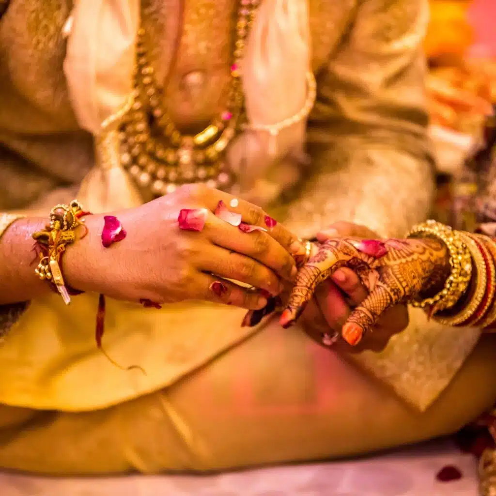 Close-up of a traditional Indian wedding ceremony where the groom places a ring on the bride’s hand surrounded by flower petals.