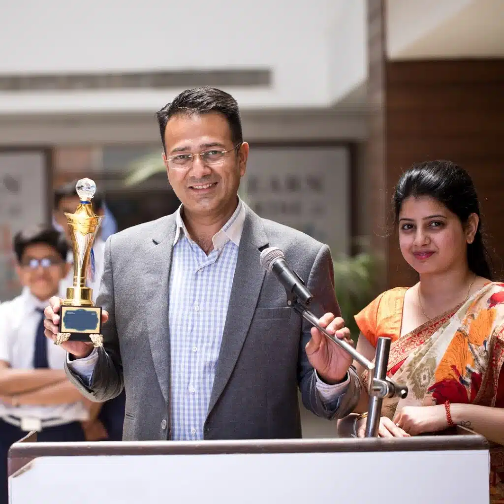 Man holding a trophy and speaking at a podium with a woman beside him during an award ceremony.