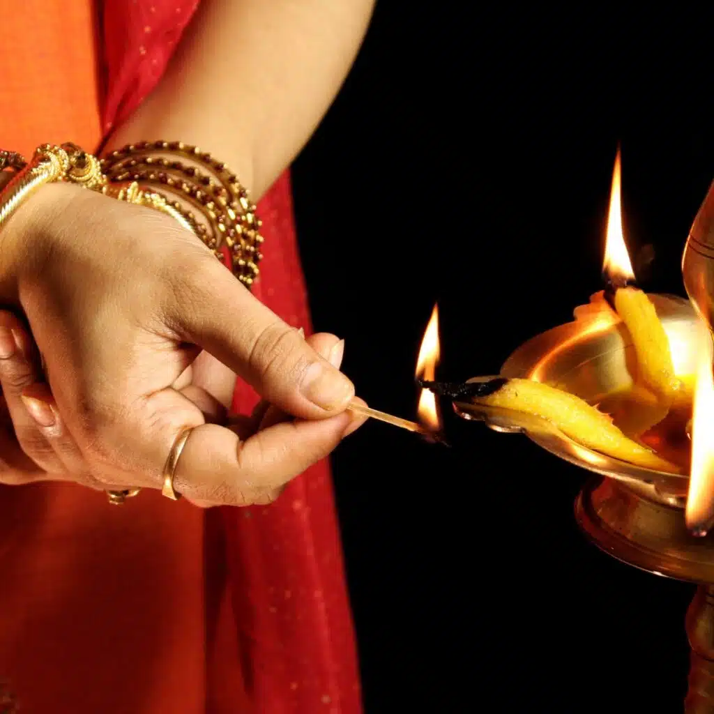 Person lighting a traditional brass oil lamp with a matchstick during a Hindu ritual or ceremony.