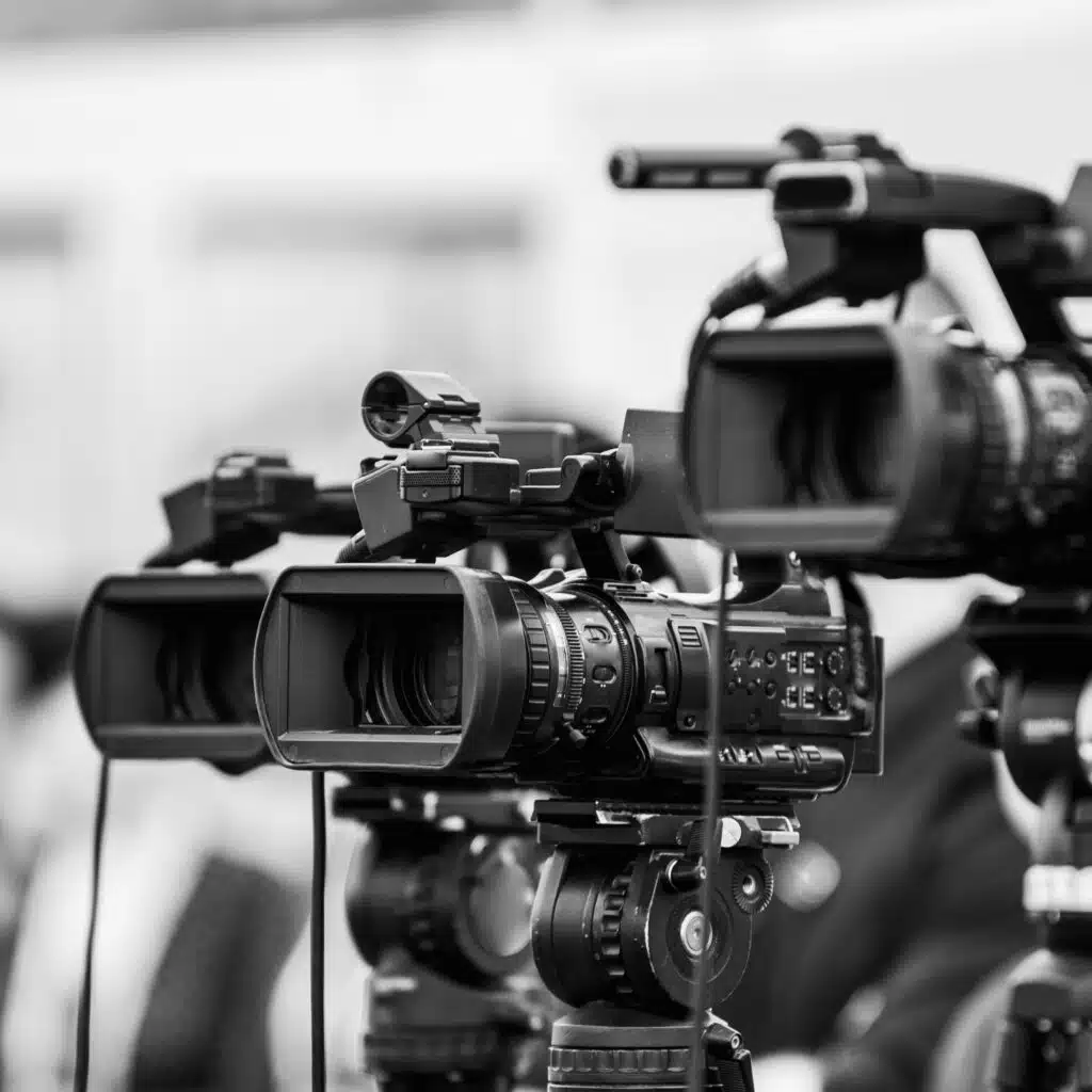 Black and white photo showing multiple professional video cameras set up on tripods, focused and ready for recording.
