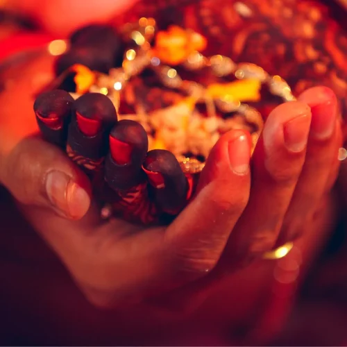Close-up of a bride’s henna-decorated hands cupping flower petals and rice during an Indian wedding ritual, lit with warm ceremonial lighting.